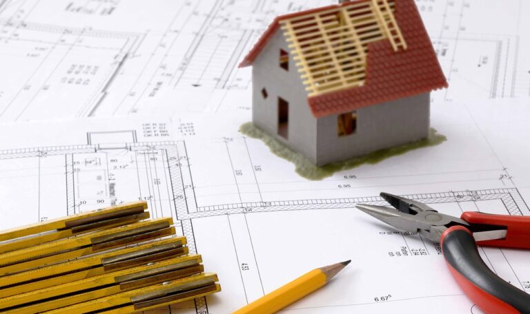 Immagine rappresentante una scrivania occupata da un progetto, un modellino di una casa in costruzione, una matita e un righello